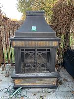 Front view of outdoor fire place showing decorative metal mesh double door and stone tile accents.