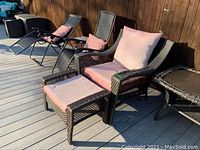Two black metal anti-gravity lounge chairs, dark brown wicker chair and ottoman with pink cushions, and wicker side table with mosaic tile top on wooden deck