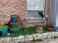 Image showing multiple planter pots with live plants against a brick wall, including forged metal garden and wall decor items scattered around. Weathered condition of items visible.