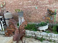 Large rusted forged metal butterfly sculpture near stone ledge and pool equipment