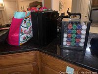 Photo showing two colorful fabric tote bags, black Samsung speaker, and black plastic case with poker chips inside.