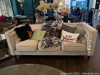 Front view of cream upholstered club style sofa with various decorative pillows and throws.