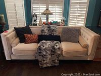 Full front view of the cream upholstered sofa with multiple throw pillows and faux fur blankets.