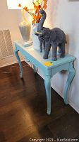 Photo showing light blue painted wood sofa table with carved legs and apron, positioned against wall with decorative items on top (not included).