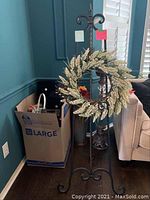 Full view of metal display stand with artificial wheat wreath hung on it, next to cardboard box containing decor items.