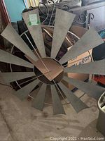 Close-up photo of large wrought iron windmill wall decor showing metal fan blades and circular design.