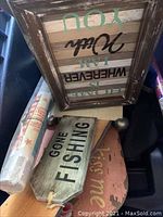 Wooden wall plaques and signs stacked together, including a green 'Gone Fishing' sign and a large wooden plaque with the phrase 'Home is Wherever I Am'.