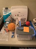Photo of assorted bathroom items including a ProCom white wall heater with control knobs, a bag of Epson salt, a yellow bath pouf, white air freshener dispenser, red candle, black pump dispenser, metal container, small glasses accessory, plastic storage container with lid, and small plastic bags.