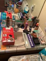 Bathroom sink counter with assorted personal care bottles, grooming products, and boxed heat wrap visible on the left side