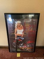 Framed poster of Budweiser poster girl sitting on red motorcycle with flame graphics.
