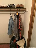 Clothing hanging including shirts and jeans, shoes and sandals on shelf above, folded clothes on floor in bags.