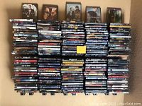 Photo overview showing stacks of DVD cases arranged in rows, visible movie titles include action, thriller, and drama genres.