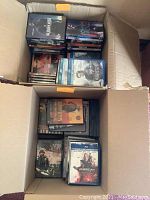 Two open boxes filled with DVDs and Blu-ray discs, showing titles such as Sleepless, John Wick, Under Heavy Fire, American, and Stand Up Guys.
