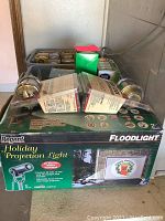 Photo of the flood lights box with two floodlight fixtures, some packaged deadbolt locks and other items on top.