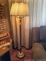 Brass floor lamp with cream pleated fabric shade in living room setting.
