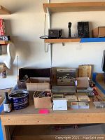 Wide view of wooden workbench with multiple boxes and containers holding drill bits, chainsaw chains, and assorted machine parts