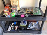 Two-tier plastic shelf with various automotive oil filters, wiring clamps, connectors, and hand tools.