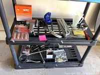 Tools and automotive accessories on black plastic shelving with air impact wrench, oil filter boxes, wrenches, a funnel, hose clamps, and screwdriver bits visible.