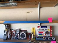 Wider image showing shelf with various tools and boxes including detail sander, modem, screw extractor, ignition tools, and sealing iron.