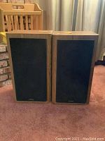 Front view of two Infinity bookshelf speakers with black fabric front grilles and wood veneer sides.