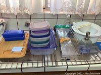 Photo showing assorted kitchen items on a tiled countertop including Tupperware containers, mixing bowls, a wooden cutting board, butter dish, soap dispenser, and tray with rack.