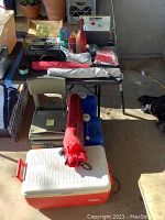 Photo of table and floor showing coolers, folding chairs, umbrellas, and outdoor gear arranged in natural light