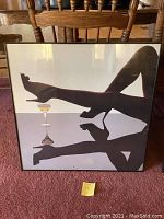 Framed print featuring silhouette of legs and champagne glass on a reflective surface.