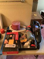 Photo showing Shark handheld vacuum, massager, pink and red candles, vacuum hose, cleaning gloves, brush, and box of vacuum bags or filters on a table