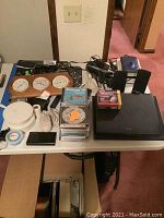 Photo depicting a table with a Sony laptop, four analog clocks mounted on wood, two black speakers, a computer mouse, a stack of CDs, and various small electronic items including a clock and cables.