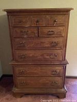 Front view of the vintage oak highboy dresser showing 7 drawers with two types of handles: round knobs on top three drawers, brass drop handles on the four larger drawers below.