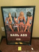 Framed vintage poster depicting four women from behind posing on a truck tailgate with bold text "HAUL ASS".