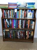 Front view of wooden 3 shelf bookcase filled with novels and Daily Guideposts books on top.