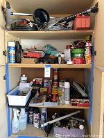Wooden shelving cabinet with multiple shelves containing automotive hoses, cables, clamps, various cans of paint and liquids, hardware items, and painting tools.