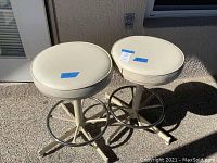 Two swivel bar stools with white round cushions and metal bases placed outdoors, showing overall condition and materials.