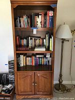 Front view of wooden bookshelf showing the three shelves filled with a variety of books and the closed two-door cabinet below.