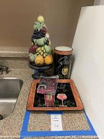 Image showing the fruit-themed decorative sculpture, wine bottle holder, cheese and wine platter with a sealed stopper on countertop next to kitchen sink