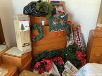 Photo of the packed and boxed 4-foot artificial Christmas tree, several wreaths, poinsettia plants, wrapping paper rolls, and gift bags arranged near wooden furniture.