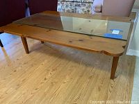 Full view of wooden drop leaf coffee table with glass top placed over the center section. Table is seen with leaves down showing narrow surface area.