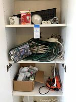 White and green extension cords, boxed electrical timer, black and orange outdoor reel light, and box of assorted plugs on shelf.