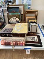 Photo showing multiple stacked photo albums and framed pictures on a white table.
