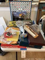 Full assortment of games including Michigan Rummy box, various boxed games like Dominoes and Tri-Ominos, and loose cards with accessories on a table.
