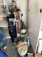 Photo showing two sets of golf clubs with all metal shafts, two golf bags, two pull carts with wheels, and a bucket of used golf balls.