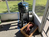 Green Patio Caddie grill with propane tank and box of parts on a screened porch.