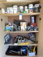 Full view of three shelves inside cabinet with labeled jars of hardware, tools, gloves, casters, and various small items.