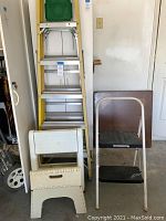 Full view of ladders and step stools in garage, shows Stanley ladder with green platform behind Safety1 and Rubbermaid stools.