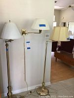 Four brass lamps including two tall floor lamps and two wall mounted swing arm lamps with white pleated fabric shades