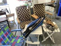 View of two woven folding lawn chairs, one colorful folding beach chair, two white folding tables, and softball equipment including bat, glove, balls, and bag on and around the tables