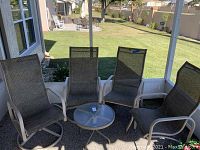 Four outdoor patio chairs and a round side table on porch showing overall set and condition.
