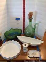 Photo showing six serving pieces on a wooden surface against a white backdrop, including green glass pitcher and bowl, white ceramic boat-shaped dish, fluted dish, small spoon rest and cup.