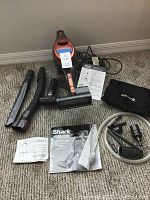 Photo of vacuum cleaner with several attachments, power cord, manuals, and storage bag arranged on carpet.